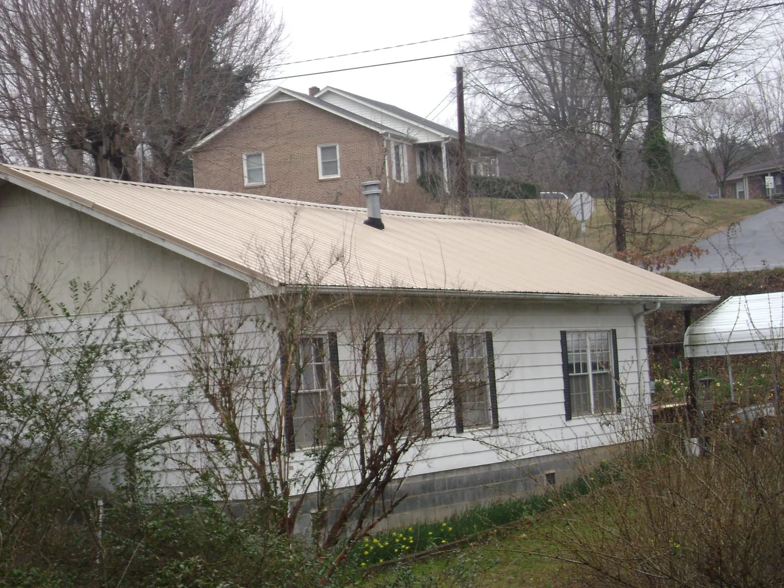 Tan metal roof on a white sided house set into a hillside in Warren