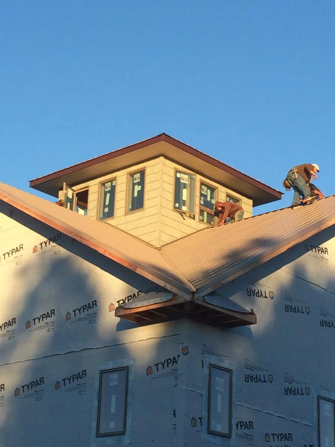 Roofers working around a rooftop cupola on a new metal roof at sunset — Roof Waterproofing in Warren by Roofing Brothers